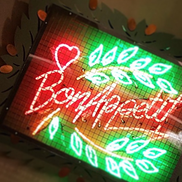 Red and green neon sign reading 'Bon Appetit'. The neon is located within a cage and is displayed on a wall. 