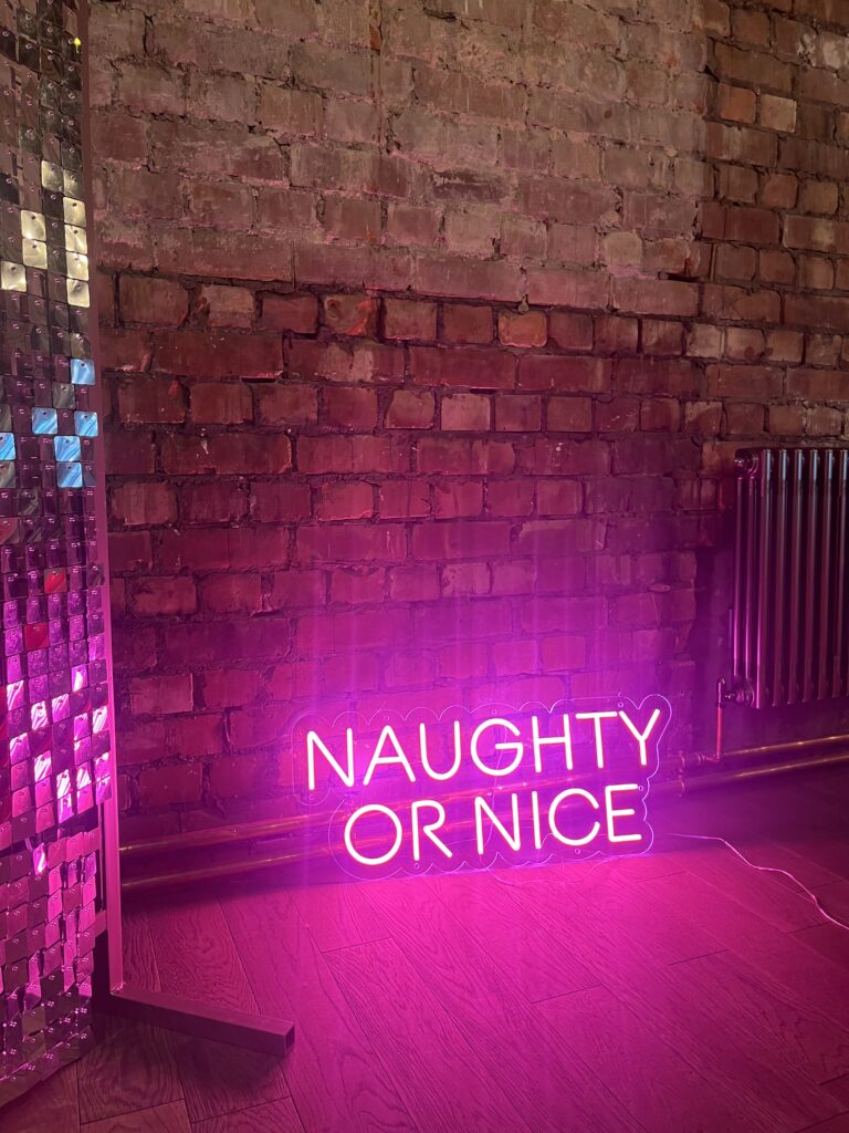 pink christmas neon sign stood against silver shimmer wall and brick wall 